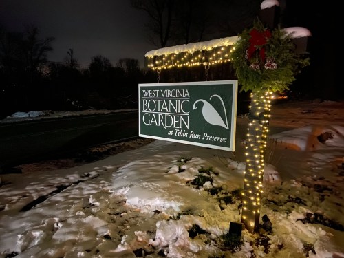 Sign for West Virginia Botanic Garden at Tibbs Run Preserve, illuminated with lights and surrounded by snow.
