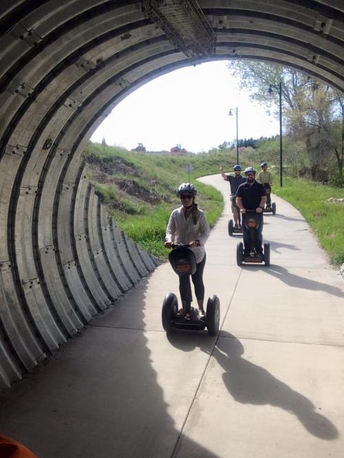 A group of people riding Segways through a tunnel on a scenic path surrounded by greenery.