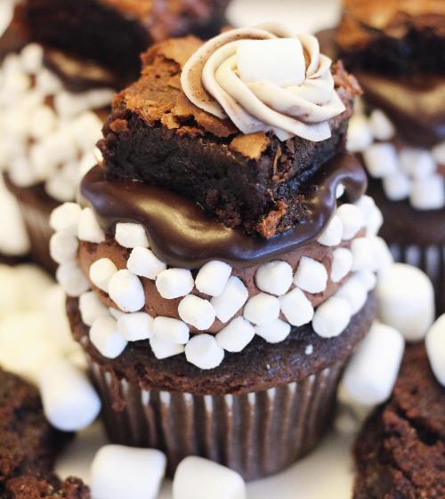 A close-up of chocolate cupcakes topped with frosting, brownie pieces, and mini marshmallows.