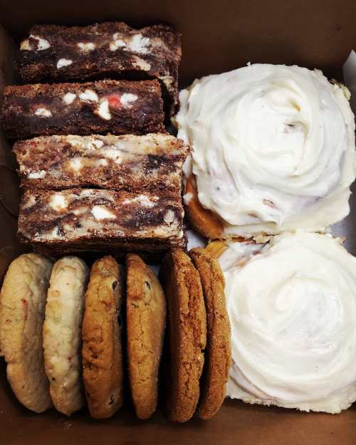 A box filled with brownies, cookies, and frosted cinnamon rolls arranged neatly.