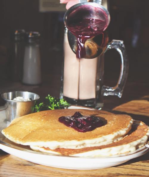 A stack of pancakes topped with berry sauce, with a glass of milkshake in the background.