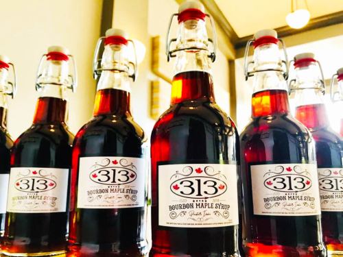 Bottles of bourbon maple syrup lined up on a shelf, featuring a label with "313" and a Canadian flag.