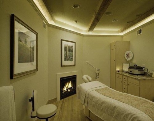 A serene spa room with a massage table, soft lighting, and a cozy fireplace, creating a relaxing atmosphere.