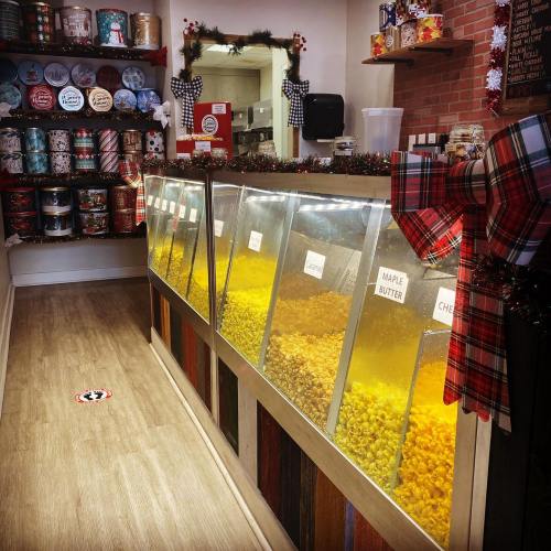 A cozy shop interior with colorful popcorn bins and festive decorations, including gift tins on the shelves.