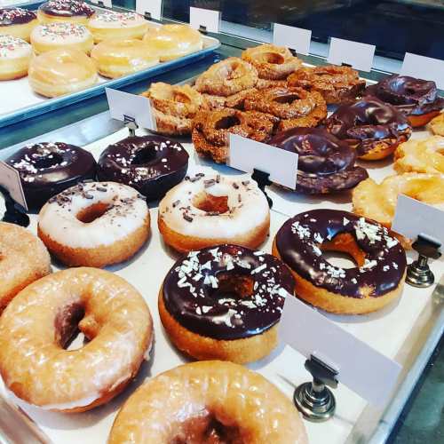 A display of assorted donuts, including glazed, chocolate, and sprinkled varieties, arranged on a tray.