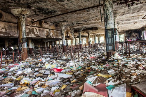 A dilapidated room filled with scattered, colorful papers and debris, showcasing peeling walls and abandoned furniture.
