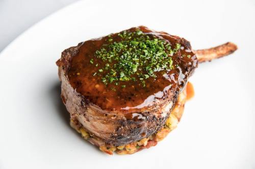 A beautifully plated pork chop topped with a rich sauce and garnished with chopped chives on a bed of savory stuffing.