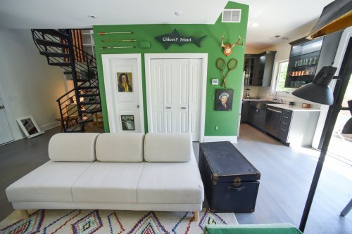 A cozy living space featuring a light sofa, green walls, artwork, and a vintage trunk, with a spiral staircase in the background.