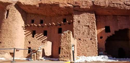 Ancient cliff dwellings made of stone, featuring windows and wooden beams, with snow on the ground.