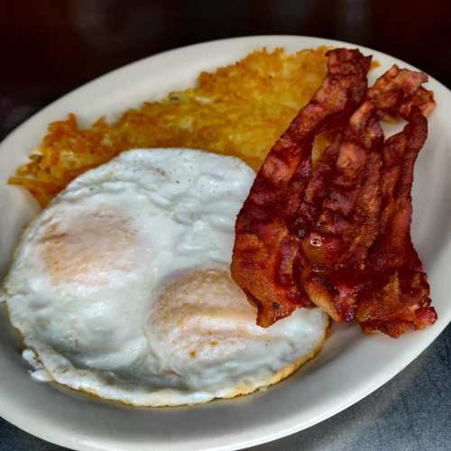 A plate with two sunny-side-up eggs, crispy bacon, and golden hash browns.