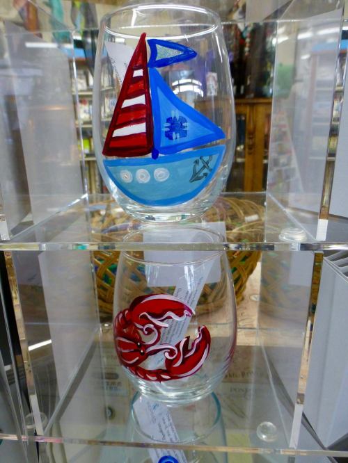 Two decorative glasses on a shelf: one with a sailboat design and the other featuring a red crab.