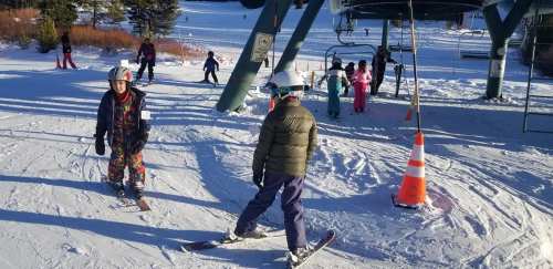 Skiers and snowboarders at a snowy ski resort, with a ski lift in the background and colorful winter attire.