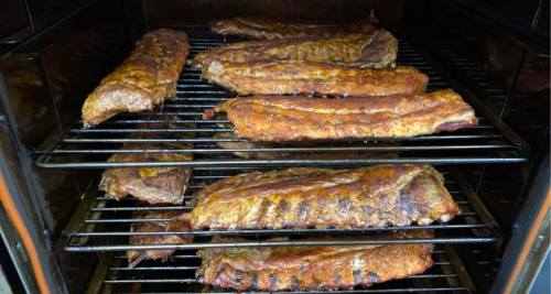 A variety of smoked ribs arranged on racks inside a smoker, showcasing a rich, golden-brown glaze.