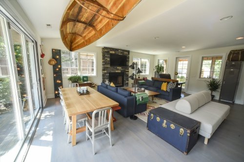 Bright, modern living space with a wooden canoe, cozy seating, a dining table, and large windows letting in natural light.