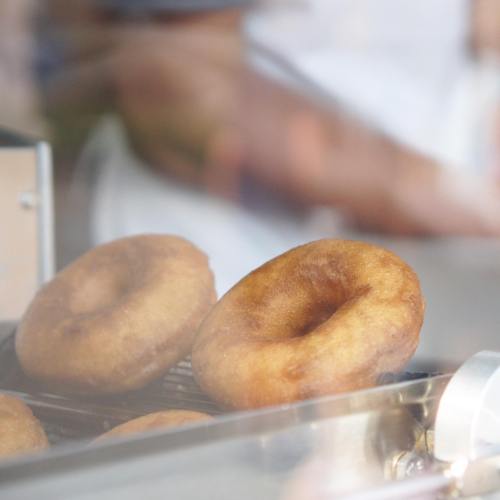 Freshly made donuts cooling on a rack, with a blurred hand in the background.