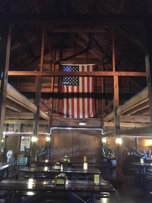 Interior of a rustic wooden restaurant with an American flag hanging from the ceiling and tables set for dining.
