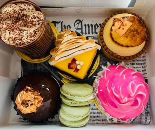 A box of assorted desserts including cakes, macarons, and a pink frosted treat, all beautifully presented.