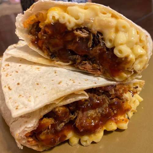 A close-up of a burrito filled with pulled pork, macaroni and cheese, and barbecue sauce, cut in half.
