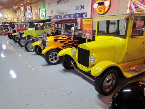 A row of vintage cars in a museum, featuring colorful designs and neon signs in the background.