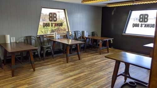 Interior of a restaurant with wooden tables, metal chairs, and large windows featuring the restaurant's logo.