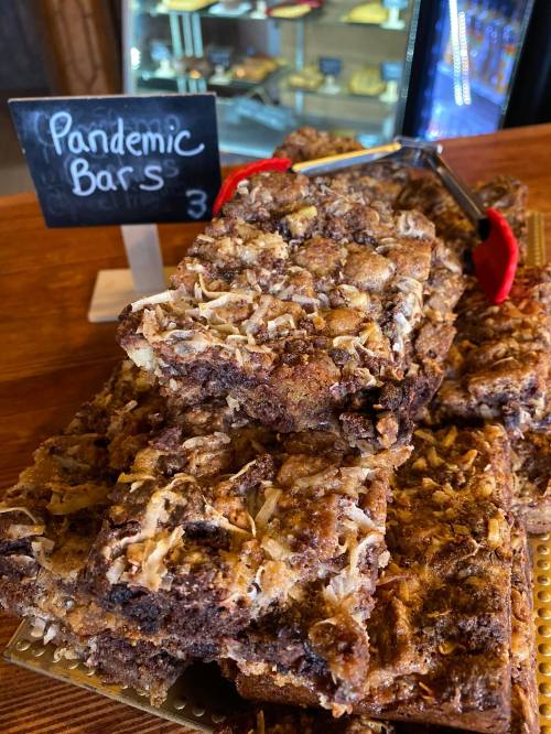 A stack of dessert bars labeled "Pandemic Bars" on a wooden counter, with a small chalkboard sign displaying the price.