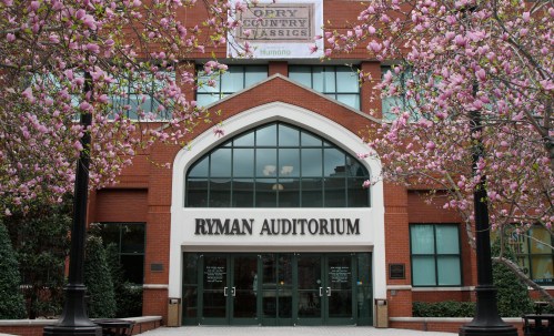Ryman Auditorium entrance framed by blooming magnolia trees and a banner for Opry Country Classics.