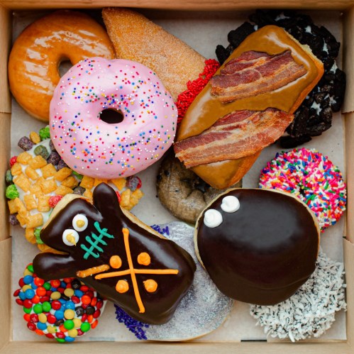 A variety of colorful donuts, including sprinkles, bacon, and unique shapes, arranged in a box.