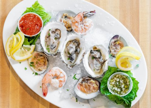 A platter of fresh oysters and shrimp on ice, garnished with lemon slices and dipping sauces.