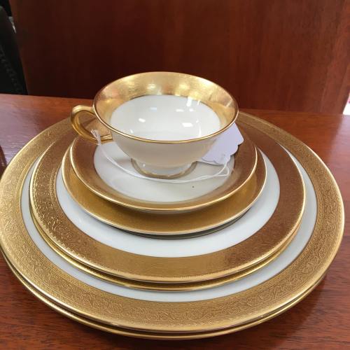 A set of elegant white and gold dinnerware, including a cup and multiple plates stacked together.