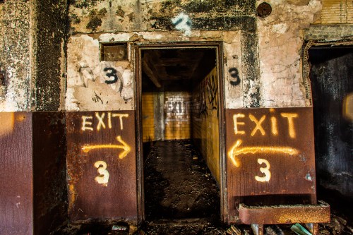 A dimly lit corridor with two doors marked "EXIT" and the number "3," surrounded by peeling walls and debris.