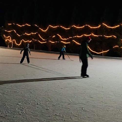 A group of people ice skating on a rink illuminated by warm string lights at night.
