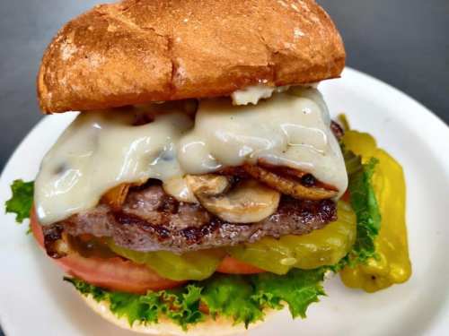 A juicy burger with melted cheese, mushrooms, lettuce, tomato, and pickles on a toasted bun, served on a plate.