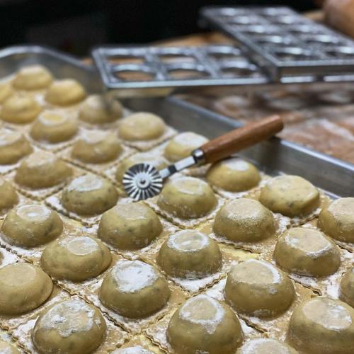 A tray of uncooked ravioli dusted with flour, with a pastry cutter resting on top.