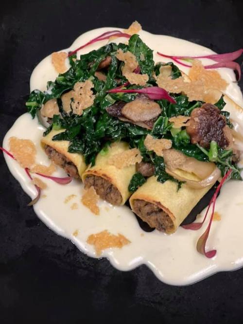 Three stuffed pasta rolls topped with sautéed greens, mushrooms, and crispy bits, served on a creamy sauce.