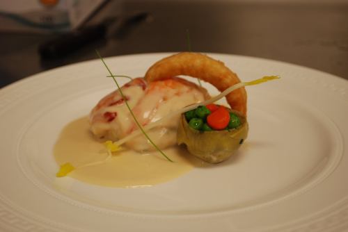 A gourmet dish featuring lobster, creamy sauce, and colorful vegetables, elegantly plated on a white dish.