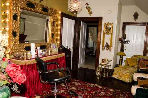 A vintage-style room featuring a large ornate mirror, a salon chair, and decorative elements like flowers and gold accents.