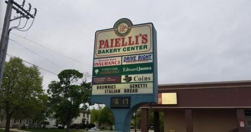 Sign for Paielli's Bakery Center featuring various businesses and services, including insurance and financial services.