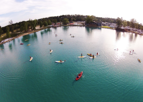Aerial view of a serene lake with people kayaking and paddleboarding on calm waters surrounded by trees.