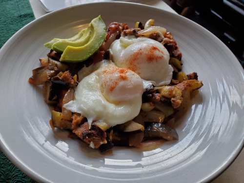 A plate of poached eggs on a bed of sautéed vegetables, topped with avocado slices and a sprinkle of seasoning.