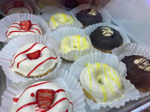 A variety of decorated donuts in white and dark chocolate, topped with colorful icing and strawberries, in paper liners.