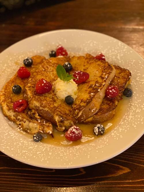 A plate of French toast topped with raspberries, blueberries, a dollop of butter, and powdered sugar.
