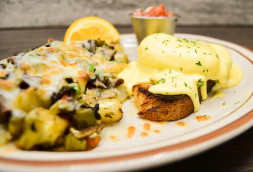 A plate of cheesy vegetable hash with poached eggs and hollandaise sauce, garnished with lemon and herbs.