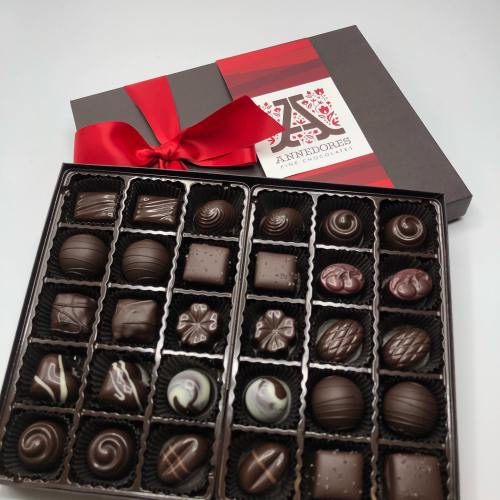 A box of assorted chocolates with a red ribbon, featuring various shapes and designs in dark and milk chocolate.