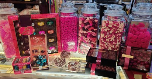 Colorful display of candies in jars, including pink hearts, chocolates, and assorted sweets in decorative packaging.
