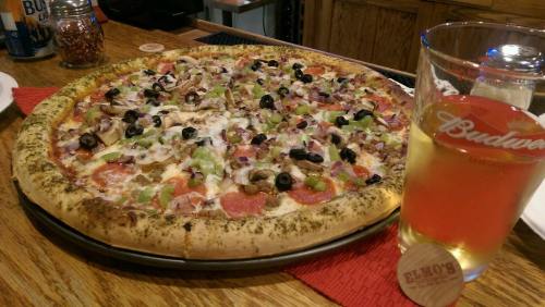A large pizza topped with pepperoni, mushrooms, olives, and green peppers, next to a glass of beer on a wooden table.