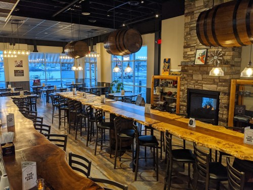 A spacious restaurant interior featuring wooden tables, a long bar, and large windows with a view. Cozy atmosphere.