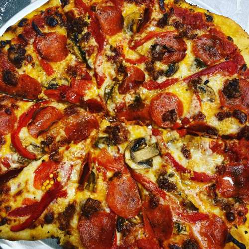 A freshly baked pizza topped with pepperoni, red peppers, mushrooms, and melted cheese, sliced into wedges.