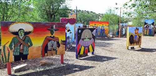 Colorful murals depicting various figures and scenes in an outdoor art installation surrounded by trees.