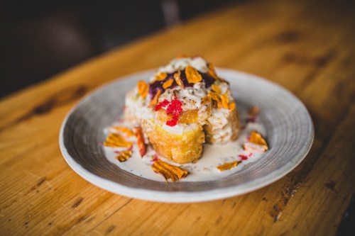 A dessert on a plate featuring layered cake topped with cream, colorful sprinkles, and crispy chips.