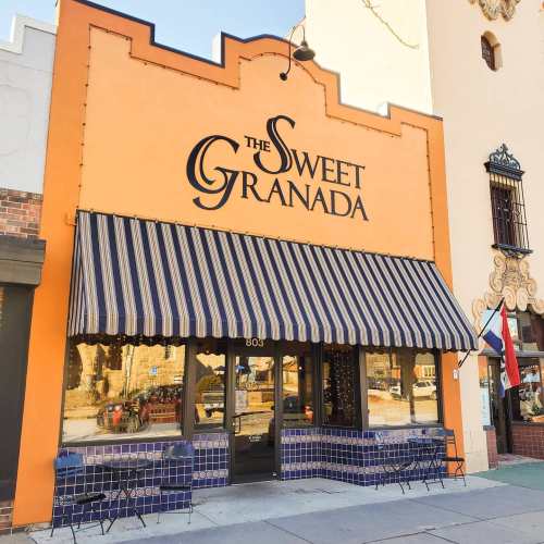 Exterior of The Sweet Granada, a vibrant orange building with a striped awning and outdoor seating.